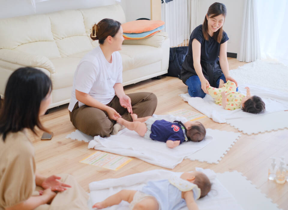 ママと赤ちゃんたちが室内で集まり、床に寝かせた赤ちゃんたちと一緒にレッスンを受けている様子。